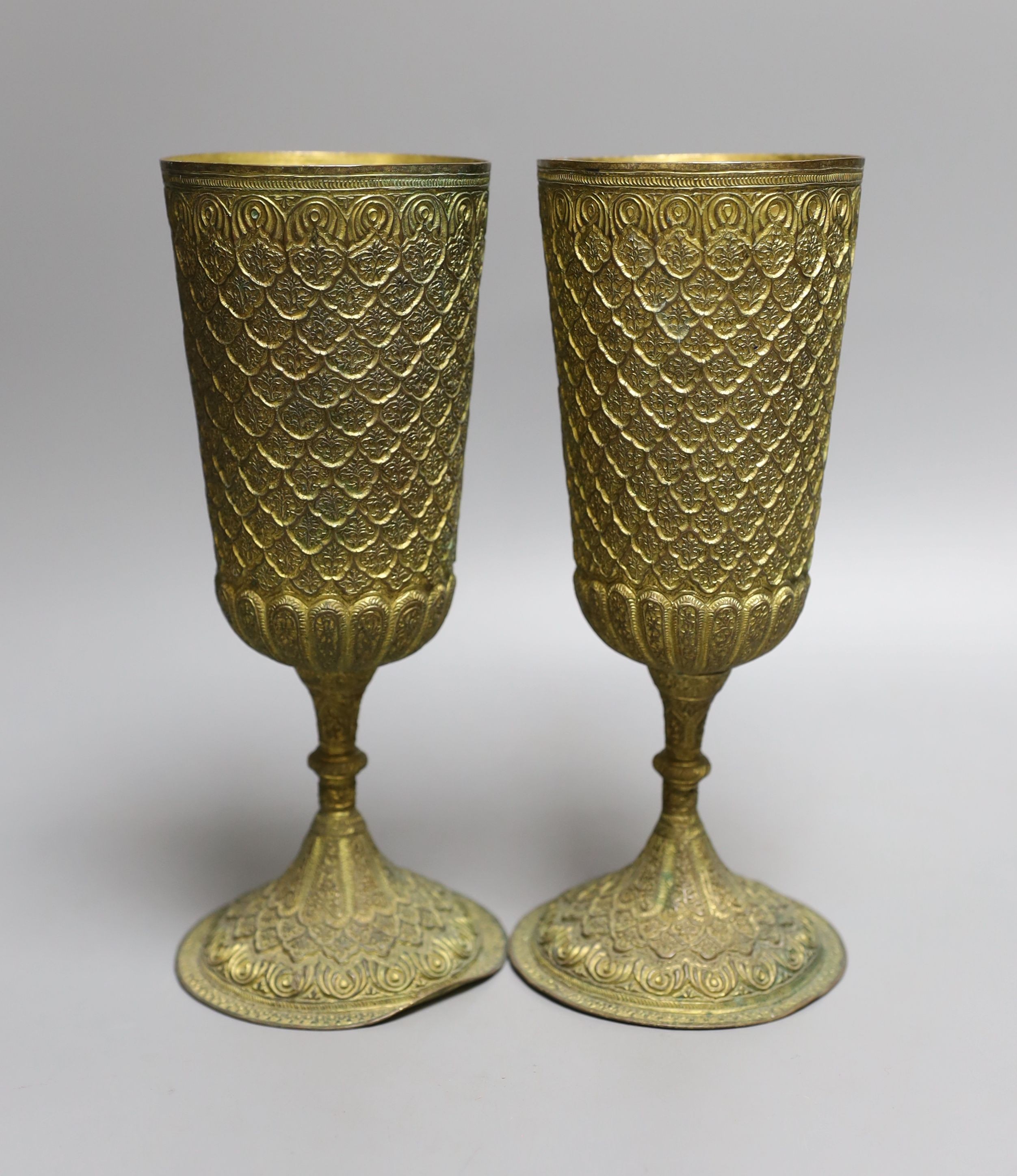 A pair of Middle Eastern repousse gilt metal goblets, 22cms high.